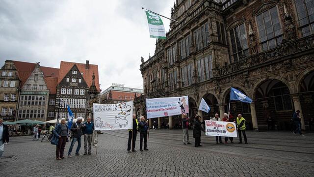 Vertreter des Bremer Friedensforums und der Ärzteorganisation IPPNW trafen sich auf dem Marktplatz, um die Beflaggung des Rathauses mit Transparenten zu unterstreichen.
