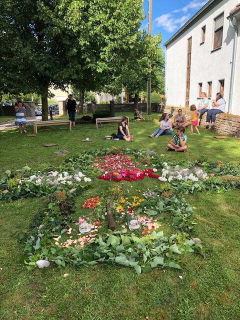 Mit Mesnerin Simone Götzfried gestalteten Kinder auf der Wiese vor der Kirche ein Ulrichskreuz in LandArt.