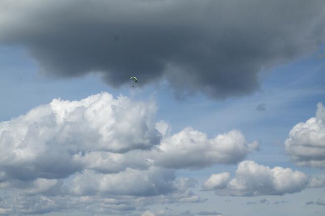 Am Rand der dunklen Wolke gleitet ein Flieger mit seinem Schirm.