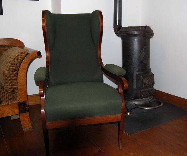 In ihr steht dieser Ohrensessel und ein moderner Kanonenofen. Beide Einrichtungsgegenstände kamen häufiger in seinen Bildgeschichten vor. So auch zum Beispiel im dritten Streich, wo Schneider Böck nach dem unfreiwilligen Bad im Bach zum Trocknen auf dem Ofen sitzt oder im vierten, wo der Ofen dem Lämpel um die Ohren fliegt als er sich die Meerschaumpfeife angezündet hatte.