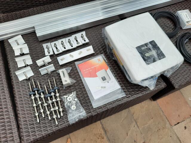 Das große Teil ist der Wechselrichter, der den Solar-Gleichstrom umrichtet zu Wechselstrom mit einer Frequenz von 50 Hertz [Hz]und der üblichen Netzspannung von 230 Volt [V]. Links daneben die Bedienungsanleitung, die großen Wandschrauben und diverses weiteres Befestigungsmaterial.