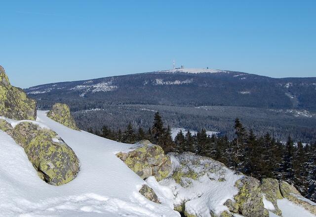 Blick vom Achtermann. Die Schneise der Brockenbahn unterhalb des Gipfelschneefeldes ist an den helleren Bereichen des Waldes erkennbar. Vom linken ist das nächste Foto entstanden.