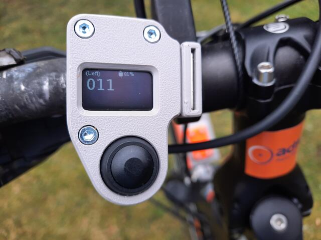 OpenBikeSensor-Taster zum Quittieren eines Messwertes, mit drei Anzeigen:  1. "(left)" = Messrichtung links, 2. "Akkustand 81 %", 3. "11" = Abstand in cm vom linken Lenkerende. Bild: http://ADFC-Langenhagen.de