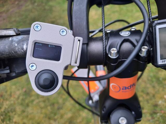 Übersichtsfoto. OpenBikeSensor-Taster zum Quittieren eines Messwertes, mit drei Anzeigen:  1. "(left)" = Messrichtung links, 2. "Akkustand 81 %", 3. "11" = Abstand in cm vom linken Lenkerende. Bild: http://ADFC-Langenhagen.de
