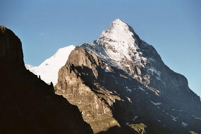Der Eiger mit Mittellegiegrat und rechts der weltweit berühmten und berüchtigten Nordwand. Im Hintergrund mit seiner weißen Ostflanke der Mönch, an dem wir bei einem Besteigungsversuch in 3800 Metern Höhe wegen eines Wettersturzes mit Hagel, Blitz und Donner einen Rückzug machen mussten.