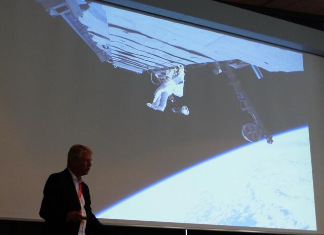 Im Umfeld der Erde ist die Raumkrümmung geringer als an der Erdoberfläche. Deswegen schwebt der Astronaut Thomas Reiter bei seinem Außenbordeinsatz an der ISS in der Schwerelosigkeit, wie er es selber erläutert, während wir auf der Erde unser Körpergewicht spüren.