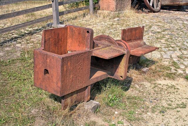 ein gußeiserner Wellkopf liegt neben der Bockwindmühle