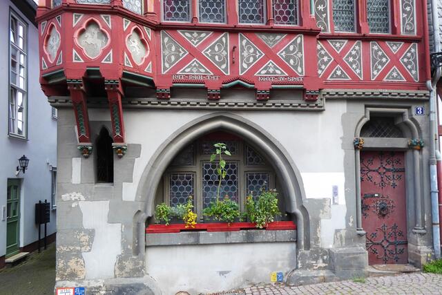 Der Jurist Carl Grimm ließ dieses Gebäude 1877 vom Architekten Carl Schäfer in der Ritterstraße als Bürohaus fertigstellen. Es ist dreigeschossig, wobei sich ein Erker mit Schopfwalmdach an der linken Seite der Hausfassade befindet, die von einem Krüppelwalmdach abgeschlossen wird. Das Bild zeigt den unteren Teil des Fachwerks über dem Erdgeschoss mit dem Sinnspruch: „Rat nach Tat kommt zu spat“. Links ist im mittleren Gefach der Marburger Reiter eingelassen, wie er sich auch im Stadtwappen wiederfindet.