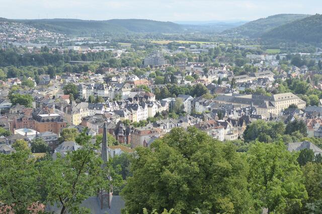 Blick in den Süden Marburgs mit der Konrad-Adenauer-Brücke und der Wohnanlage, die als Affenfelsen bekannt ist. Sie steht dort, wo einst das Wirtshaus an der Lahn stand. Rechts steht der Block des Staatsarchivs Marburg. Vorne ragt der Turm der Kugelkirche in die Höhe.