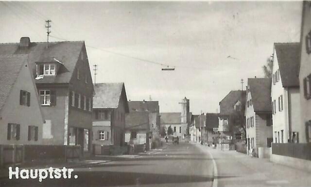 Das Bild einer Ansichtskarte aus dem Jahr 1960 zeigt weitere Veränderungen. Die Straße ist nun asphaltiert (zuvor gepflastert). Das hohe Haus links hat im Erdgeschoss einen Laden. Die Straße hieß damals übrigens bereits Donauwörther Straße. Die Beschriftung „Hauptstraße“ beschreibt die Funktion der Straße, nicht ihren Namen.
Das Bild stammt von einer Ansichtskarte (1960)