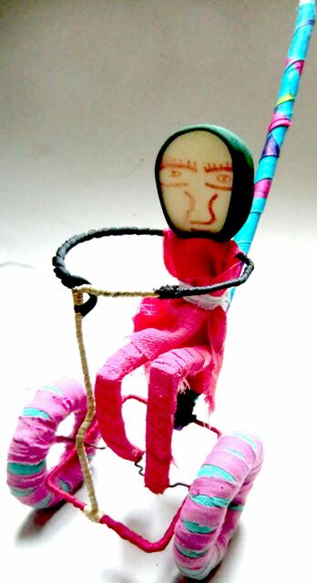 Hoppla, hier komme ich: ein Upcyclingkunstwerk eines afrikanischen Kindes, das am Stock geschoben mit den Beinen strampelt und das lustige Gefährt antreibt