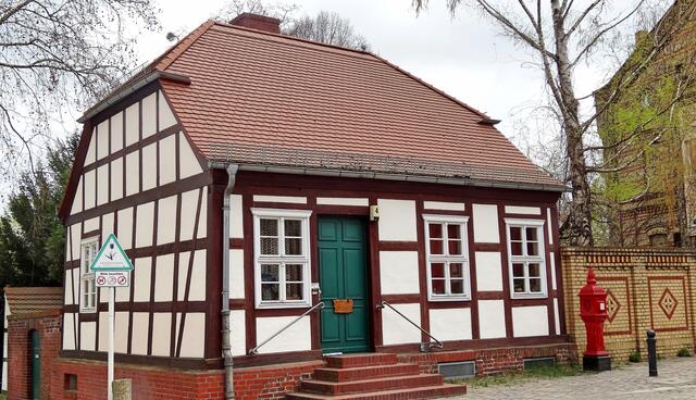 Straße am Behnitz. Das Fachwerkhaus Haus-Nr. 4 stammt etwa aus der Mitte des 19. Jahrhunderts. Zwischen diesem und dem Nachbarhaus zur linken Hand führt ein schmaler Weg hinunter zur Havel und an die Schleuse. Früher sollen an dieser Stelle die Spandauer ihr Vieh ans Wasser getrieben haben. Rechts vor dem Haus ein roter antiker Feuermelder.