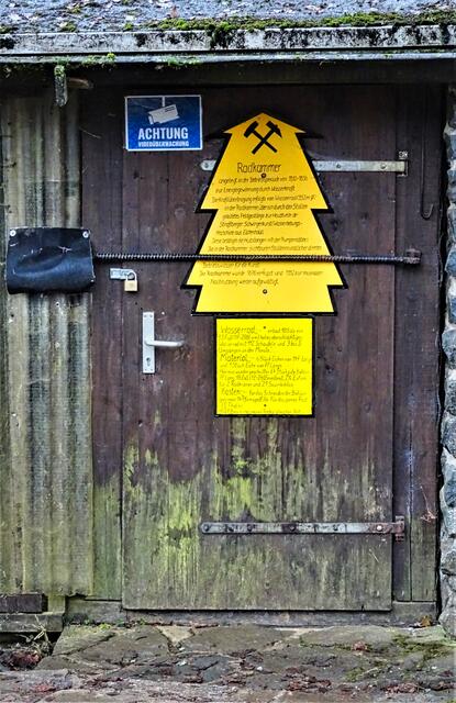 verschlossene Tür der Glasebacher Radstube, durch das Anheben der schwarzen Lederklappe kann man einen Blick in die Radstube werfen