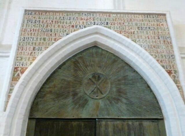 Inschrift über dem Bronze-Portal - ST. KATHARINEN 1350-1420 ERBAUT - IM KRIEGE 1943 ZERSTÖRT - WIEDERAUFGEBAUT 1956 - GEWEIHT ALS DR. KURT SIEVEKING BÜRGERMEISTER WAR UND PROF. D. VOLKMAR HERNTRICH BISCHOF DER EVGL. LANDESKIRCHE + HAMBURG ...