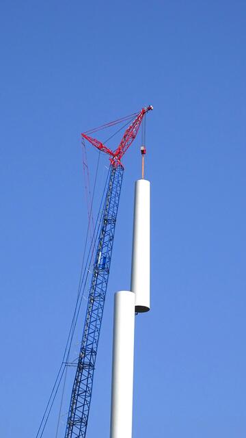 Schwerlastkran (bis zur Spitze rund 270 Meter) hebt das dritte Stahlrohr als letztes Teilstück des Turms ...