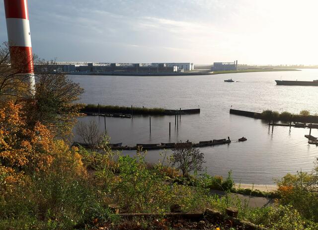 Blick auf den Mühlenberger Leuchtturm bis zu den Airbus-Werken und  im Vordergrund auf einen Schleppzug im Hafenbecken.
