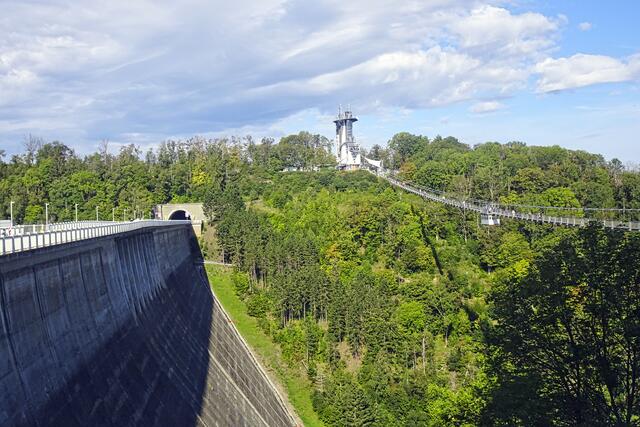 links die 98 m hohe Staumauer mit dem Tunnel, rechts die 458 m lange Hängeseilbrücke, in der Mitte der Absprungcontainer für den Pendelsprung