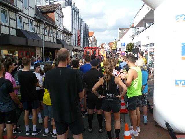 Die auf den Start wartenden Teilnehmer/innen der 10er-Strecke  und Zuschauer werden vom Moderator Christoph Dannowski aufgefordert, die Straße zu verlassen. 
