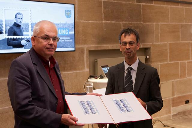 In Vertretung von Minister Christian Lindner überreichte Martin Chaudhuri (rechts) vom Bundesfinanzministerium eine Dokumentenmappe mit den Trautmann-Sonderwertzeichen an Ekkehard Lentz von Tura Bremen.  | Foto: Karl-Friedrich Hohl, Stadt Nürnberg