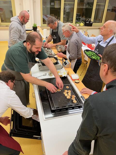 Starkoch Johannes Steichele zeigt, dass man Jakobsmuscheln ganz heiß kurz anbraten muss und dass diese vorher trocken getupft werden sollen. In die heiße Pfanne etwas Zitronenschale und ein kleines Stückchen Vanilleschote. Danach nur mit Pfeffer und Fleur de Sel würzen. Im Hintergrund werden die Vorspeisenteller mit Büffelmozarella vorbereitet.