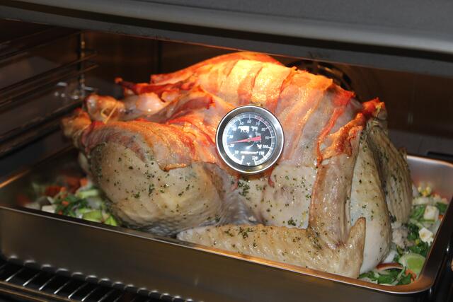 Mit dem Thermometer wird hier die Kerntemperatur gemessen 24°, das heißt, das dauert noch lang. Dass das "Vögelein" nicht zu trocken wird, hat man es mit Räucherspeck belegt, der auch noch einen guten Geschmack reinbringt.