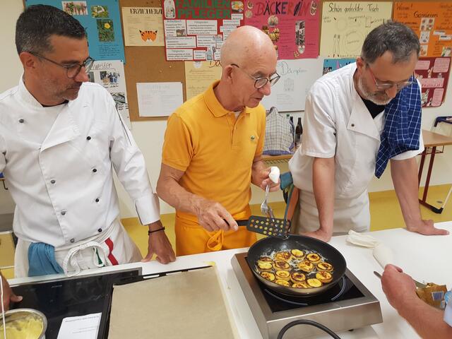 Claudio Erdner (links) beobachtet ob Klaus Hill die Blinis richtig brät, während Alois Moosmüller im Rezept liest. 