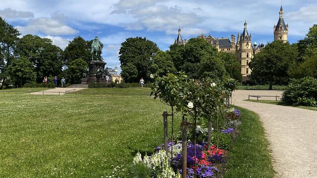 Von den Bänken der Gartenanlage reicht die Sicht über die bunten Blumenbeete auf das historische Reiterdenkmal und das prächtige Schloss auf der Insel des Schweriner Sees. Foto: Helmut Kuzina
