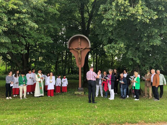 Foto: Vor dem Speckkreuz stehen die Lektoren, die Ministranten, Pfarrer Norman D´Souza und der Kirchenchor mit Leiter Konrad Eser. 