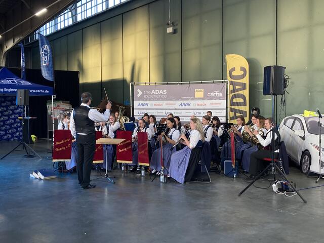Das Blasorchester Penzing beim ADAS Experience zwischen Auto-Dummy (rechts) und Infoständen im ehemaligen Flugzeug-Hangar. | Foto: Natalie Golowko/carhs.training
