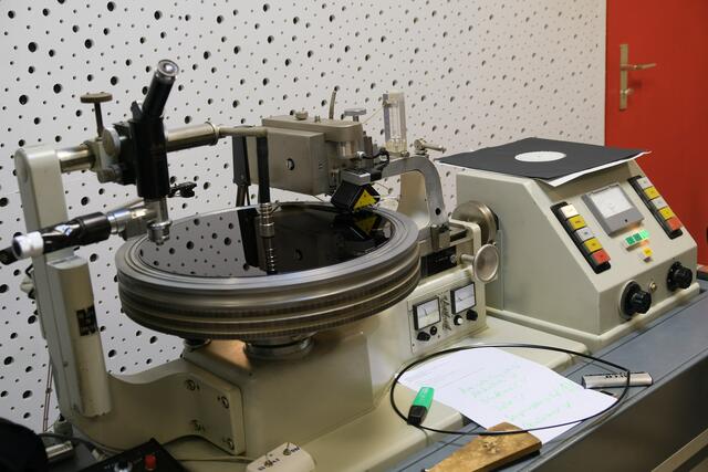 Die unbeschnittene Masterplatte liegt auf. Die Platte dreht sich und der Schneidekopf senkt sich herab und schneidet die Tonspur in die Platte. 