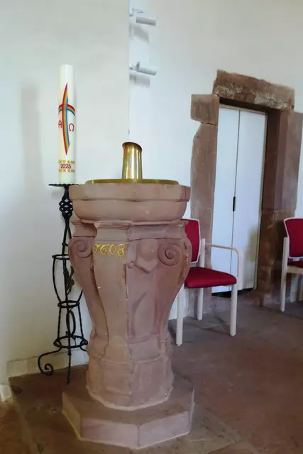 Der Taufstein aus Sandstein, dessen Becken vier oben in Voluten auslaufende Pilaster einfassen, nennt das Jahr „1608“. 