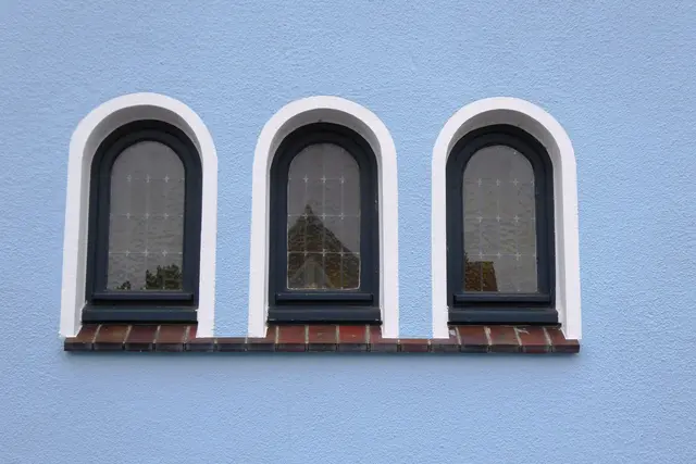 Blaue Hauswand mit drei Fenstern.