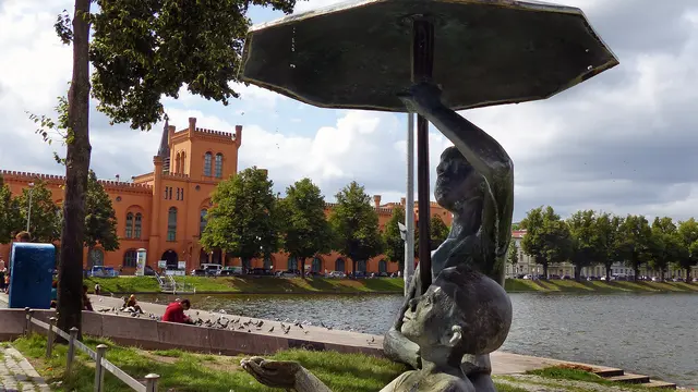 Im Hochsommer nutzen die „Schirmkinder‟ des Bildhauers Stephan Horota am Südufer des Pfaffenteichs ihren Regenschirm, aus dem es stets leicht tropft, als Schutz gegen den strahlenden Sonnenschein. Viele nehmen das Motiv dieser Bronzeskulptur als Erinnerung an den Hauptstadtbesuch per Selfie mit. Foto: Helmut Kuzina