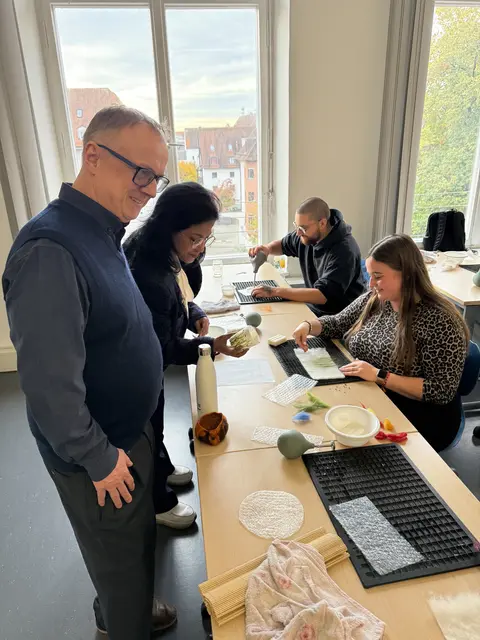 Besuch am Staatsinstitut für die Ausbildung von Fachlehrern Augsburg - R. Heider und S. Gupta im Gespräch mit einer Studentin zu einem Unterrichtsprojekt im Fach Werken/Textilarbeit.