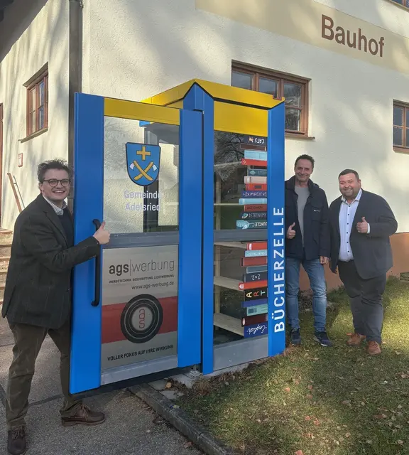 Begrüßt von Dorffarben und Gemeindewappen macht die Bücherleihe noch mehr Freude – Bürgermeister Bernhard, Thomas Glass und Ludwig Lenzgeiger inspizieren die renovierten Bücherzellen.