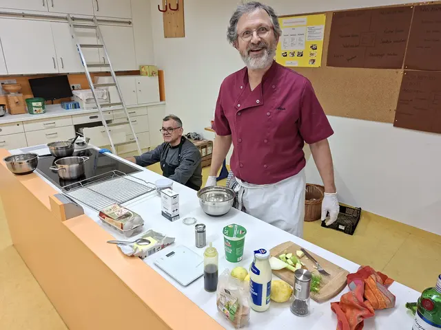 Dr. Alois Mossmüller steht hier vor seinem Stammplatz in der Schulküche, die letzte Kochzeile. Hier bereitet er meistens die köstlichen Nachspeisen zu. Küchenmeister Jürgen Rohm kontroliert gerade die Nudelrösti im Backofen. | Foto: Otto Killensberger