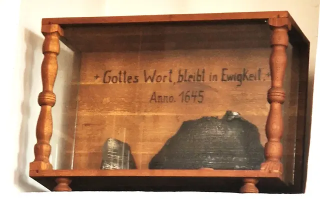 Schaukasten mit Resten der beim Kirchenbrand 1973 geschmolzenen Bronzeglocke aus dem Jahr 1645.
         in Erinnerung an die Glocke von 1645 mit der Aufschrift
                            „verbum domini manet in eternum“
