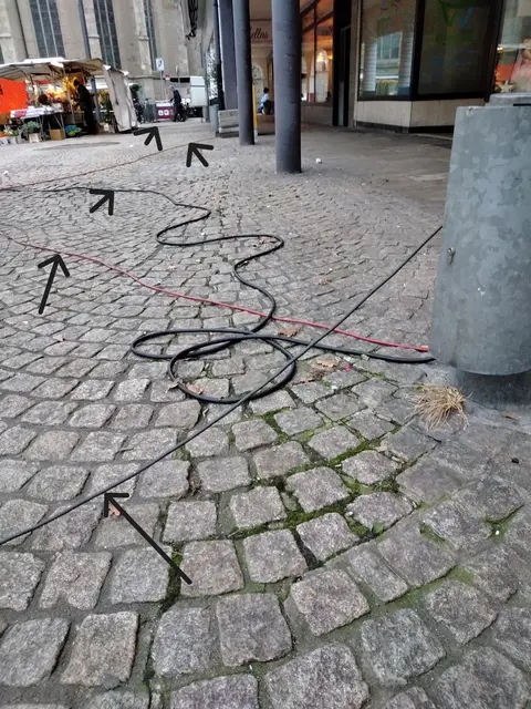 Mehrere kreuz und quer, lose über den Boden in Schlaufen verlegte Stromversorgungskabel (schwarze Gummischlauchleitung) auf dem Marktplatz "Großer Markt" in Wesel.
Sachstand: Mittwochmarkt 11.12.2024
Kabelanzahl siehe Pfeilmarkierungen | Foto: Siegmund Walter, 11.12.2024, 09:33 Uhr