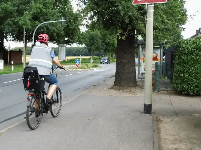 Radfahrerin mit Kindersitz auf dem Gepäckträger auf dem gemeinsamen Fuß- und Radweg an der Brüner Landstraße, Ecke Brömderweg.
Vor der Radfahrenden, zwei,- genauer gesagt, drei Hindernisse, wenn man die durch das Wurzelwerk schräg-gestellten Pflastersteine mit einbezieht: Ein dicker Baum mitten auf dem Fuß- und Radweg, kurz dahinter seitlich eine Bushaltestelle mit seitlicher Plakatierung, die ev. zur Sichtbehinderung führen könnte, weil sich kurz dahinter eine Seitenstraße befindet, und zwar der Brömderweg aus dem jederzeit andere Verkehrsteilnehmer kommen könnten und denen selbst die Sicht durch die vorgenannten Hindernisse genommen wird.
Sachlage: 27.07.2025 | Foto: Siegmund Walter, 27.07.2025, 16:29 Uhr
