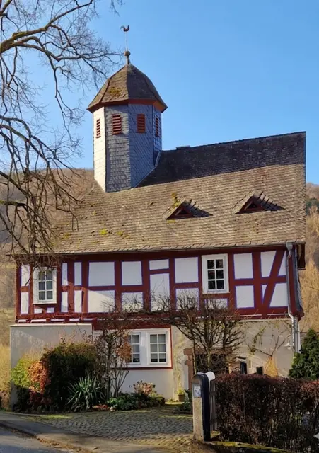 Die ehemalige Kapelle wurde 1592 gebaut[1]. Sie wurde zwischen 1789 und 1792 durchgreifend erneuert und 1982 zum Wohngebäude umgebaut.
Glocke  (0,68  Dm.,  190  kg).  Inschrift  Antiqua- 
Versalien:  AUS  DEM  FEUER  FLOS  ICH  HANS  KERLE  IN  F.  F.  (Frankfurt) 
GOS  MICH  1600. 
Diese Glocke befindet sich jetzt in
Der Friedhofskapelle von Breidenstein
