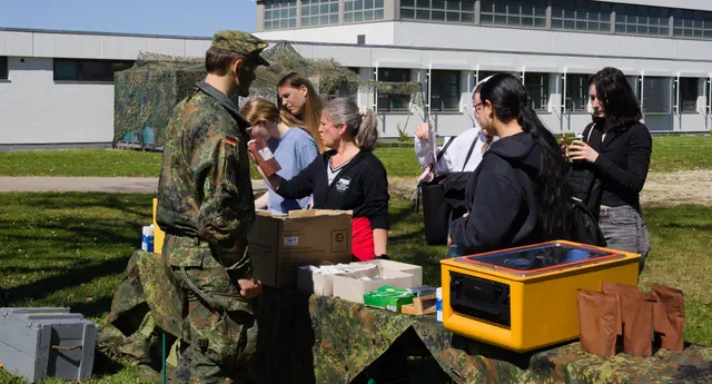 Zivilistinnen begutachten an einem Stand der Bundeswehr braune Beutel mit Einpersonenpackungen (EPa).