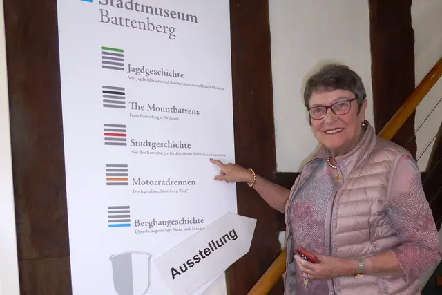 Elisabeth Skupin vor dem Wegweiser zu den Abteilungen Stadtgeschichte, Familie Battenberg (Mountbatten), Bergbau, Jagd und Motorradrennen "Rund um Battenberg" im Stadtmuseum Battenberg. 