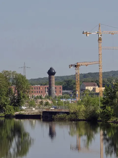 Der markante, dunkle Wasserturm ist ein historisches Relikt des ehemaligen Rangierbahnhofs Wedau.Im Vordergrund ist einer der Seen der Sechs-Seen-Platte zu sehen, an denen das neue Wohnquartier entsteht.