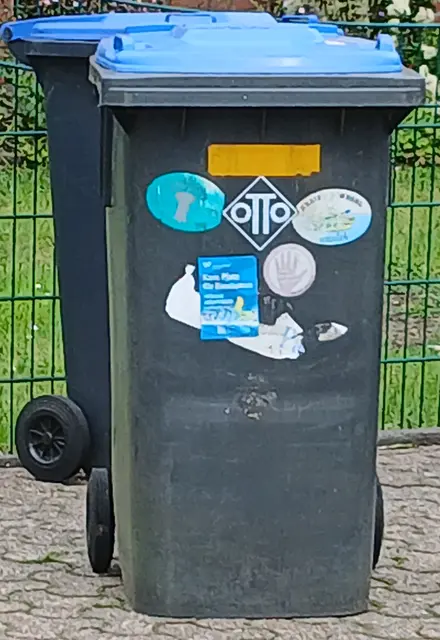 Mit Aufklebern beklebte Tonne für Papier und Pappe. 
Ort: Wesel
Rechtliche Lage: Grundsätzlich ist das großflächige Bekleben der ASG-Mülltonnen mit privaten oder werblichen Aufklebern nicht erlaubt, da die Tonnen im Eigentum der Stadt Wesel7des ASG stehen. Kleine, dezente Aufkleber zur Zuordnung (Hausnummer/Name) oder rein informative Mülltrennungssymbole werden in der Praxis aber meist toleriert. | Foto: Siegmund Walter, 20.05.2026