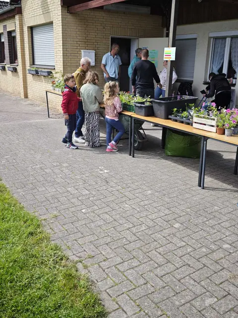 Im Vordergrund stehen Gäste an einem Tisch mit Pflanzen. Im Hintergrund spricht Manuel Diefert mit Vorstandsmitgliedern des KGV Dornröschen.