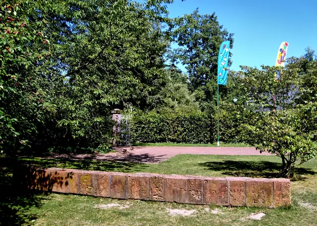 Mitten auf der Wiese steht die Ton-Mauer "Über Stock und Stein" von Titus Grab und Johannes Volkmann (1996). In die Ton-Platten haben die Kinder mit Stöckchen und Steinen Reliefs gemalt.
Im Hintergrund: Inken Bojen, Fahnen und Maste (2007). | Foto: copyright Margot Klütsch