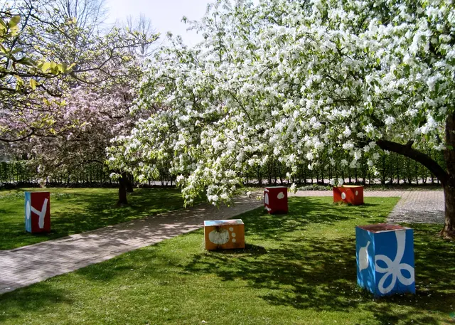 Im Garten ergeben die bunt lackierten Metallwürfel einen wunderbaren Kontrast zu den blühenden Bäumen. Gleichzeitig nimmt die farbenfrohe Bemalung der Kuben Naturformen auf (Achmed Ibrahim, 2002). 
 | Foto: copyright Margot Klütsch