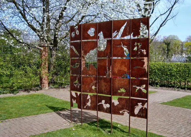 Mitten im Garten steht der Paravent aus inzwischen angerosteten Blechtafeln mit ausgestanzten pflanzlichen Motiven. Durch sie betrachtet man die Natur als Lichtbilder (Christian Bauer, 1996). Umgekehrt wirft der Paravent ein Schattenbild auf die Wiese.  | Foto: copyright Margot Klütsch