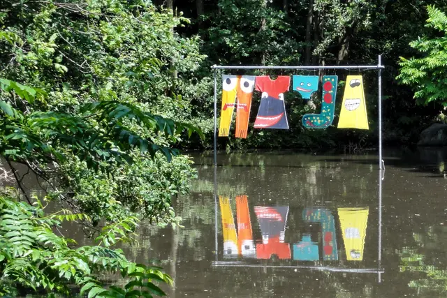 An der Insel im Düssellauf steht eine riesige Wäschestange, behängt mit bunten Wäschestücken. Die Wäsche des fiktiven Bewohners scheint Grimassen zu schneiden (Carl Hager: Große Wäsche, 2014). | Foto: copyright Margot Klütsch