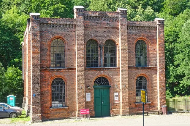 Im Jahre 1827 wurde das Carlswerk gegründet. Die im Bild zu sehende ehem. Maschinenfabrik wurde im Jahre 1865 in Betrieb genommen. Sie hatte sich auf die Herstellung von Sondermaschinen spezialisiert. Nach 1945 erfolgte dort die Produktion von Gasgeräten. Die Stilllegung erfolgte erfolgte Anfangs der 90 - er Jahren des 20. Jahrhunderts. Heute ist das Gebäude ein Hüttenmuseum.